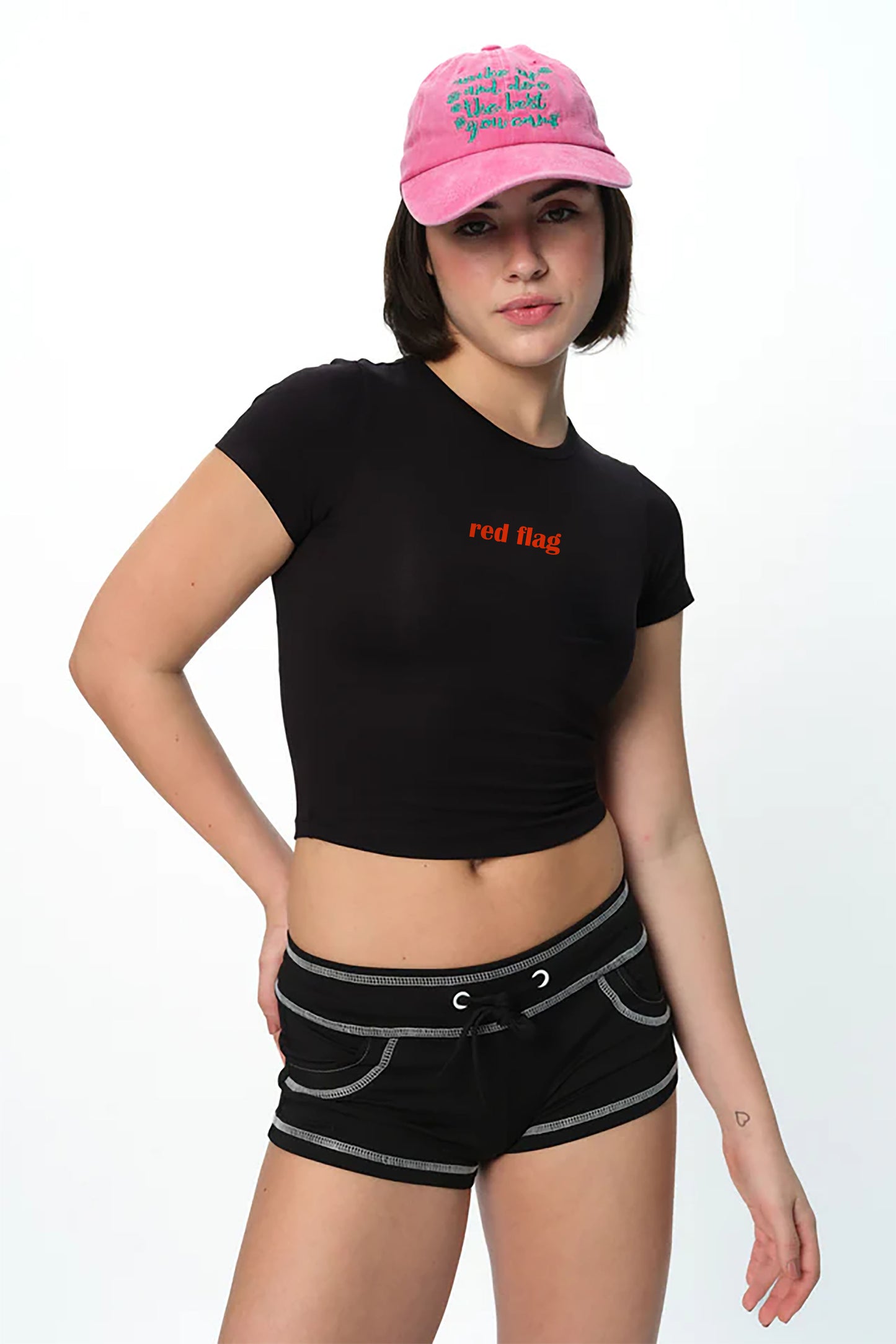 spankers Woman wearing a black crop top with text, black shorts, and a pink cap on a white background
